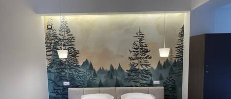 A hotel room with a bed, a large wall mural, a wardrobe, and a hanging light fixture.