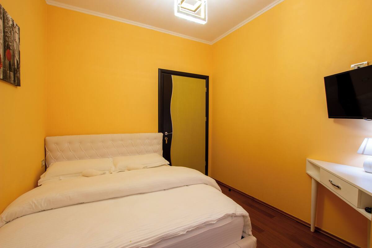A room with a bed, a desk, a television, and a door.