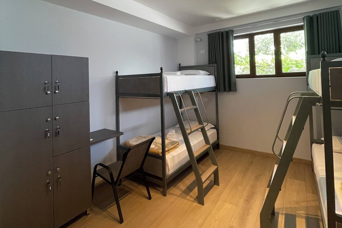 A bunk bed room with a wardrobe, a window with curtains, and a wooden floor.