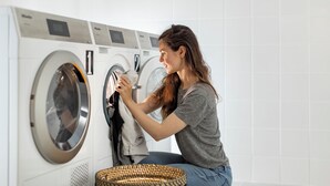 A person loading clothes into a front-loading washing machine in a modern laundry room with white tiled walls. - Apparteo Montpellier (Montpellier)