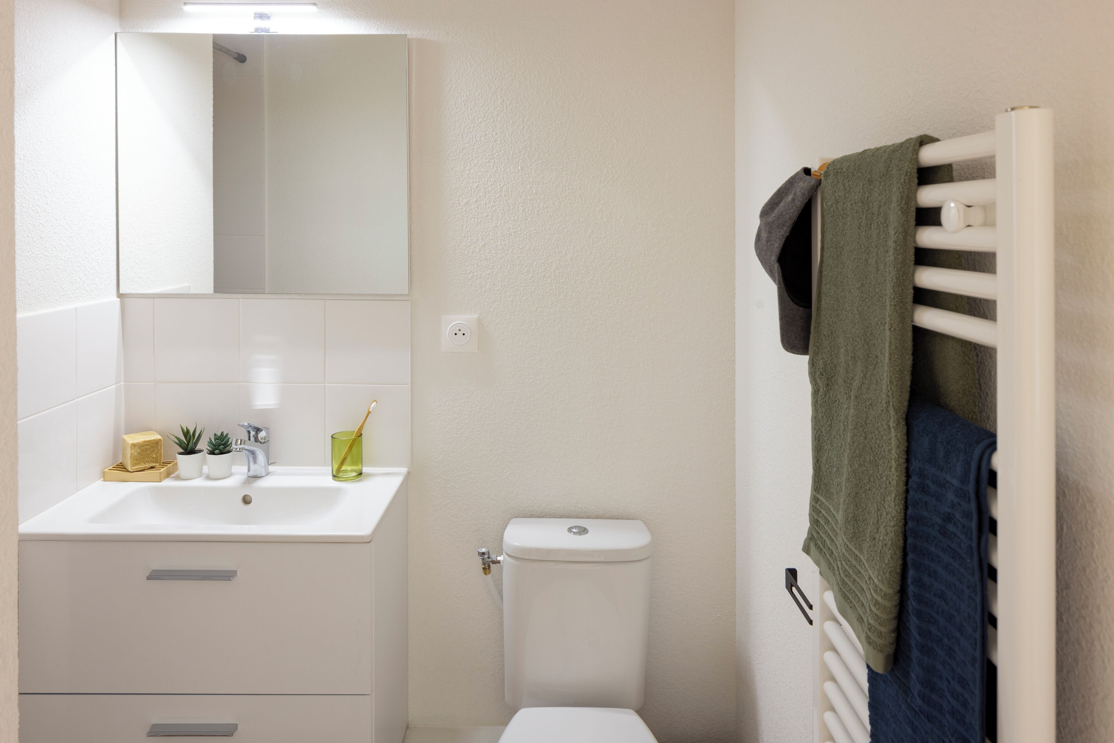 Un baño con lavamanos blanco, espejo, inodoro y toallero.