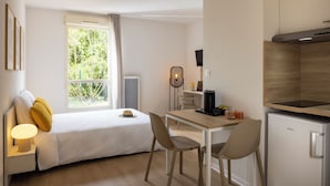 A modern hotel room with a bed, bedside table, lamp, and a view of greenery through the window. - Apparteo Montpellier (Montpellier)