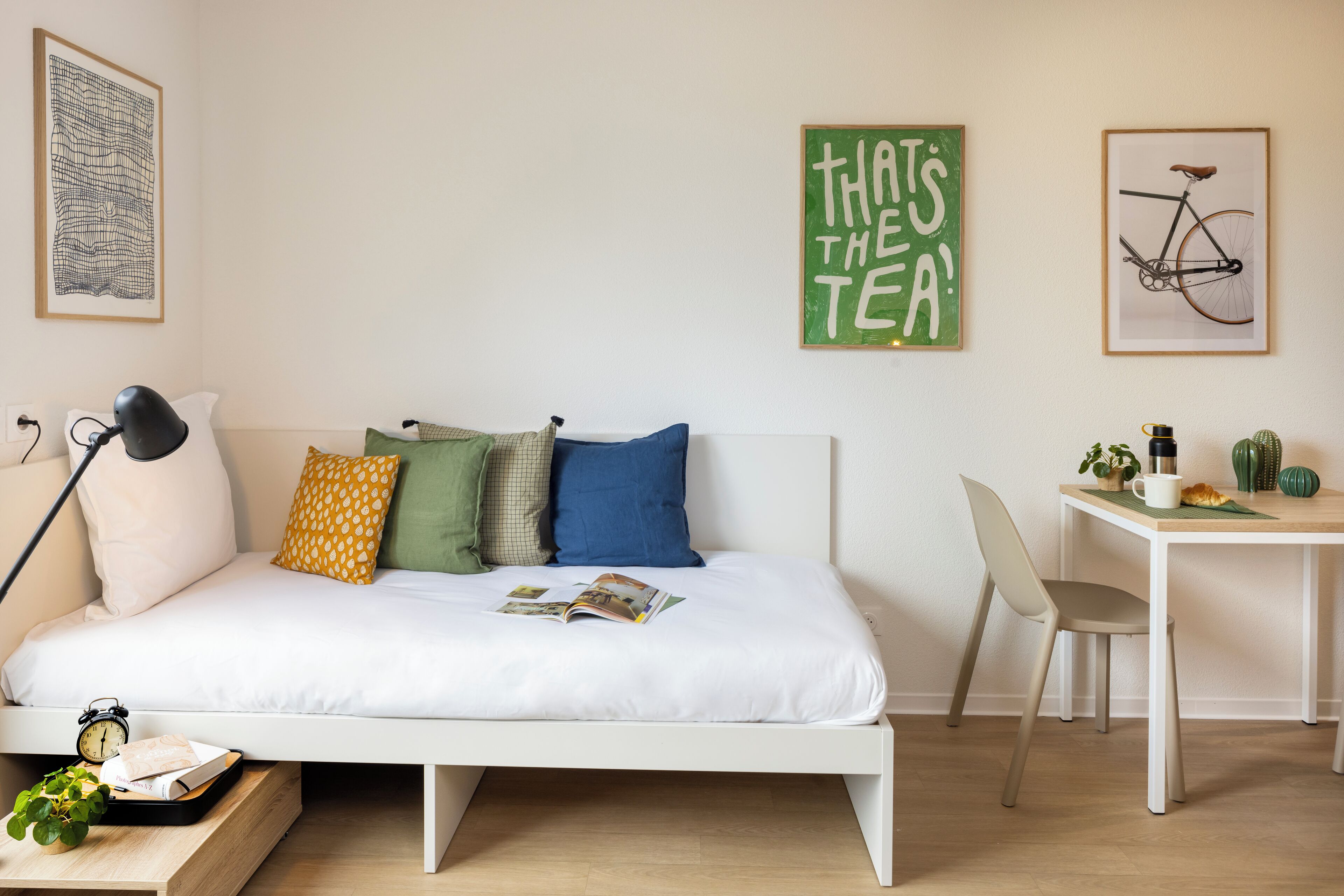 Een keurig opgemaakt slaapkamer met een bed, nachtkastje, lamp, en een klein bureau met een stoel.