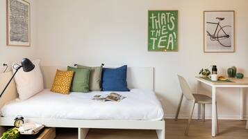 Een keurig opgemaakt slaapkamer met een bed, nachtkastje, lamp, en een klein bureau met een stoel.