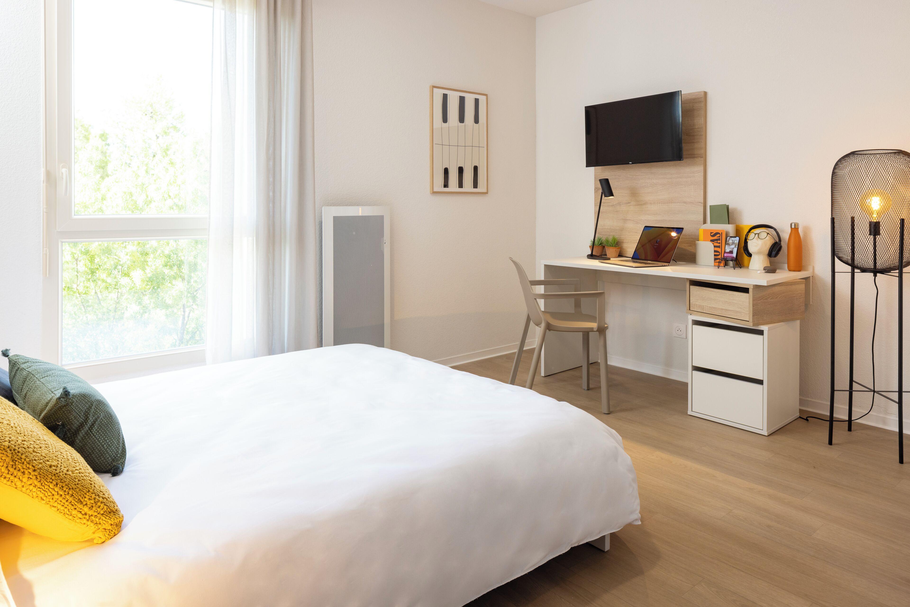 Une chambre d’hôtel équipée d’un lit, d’un bureau avec un ordinateur, d’une chaise, d’une télévision et d’une lampe.