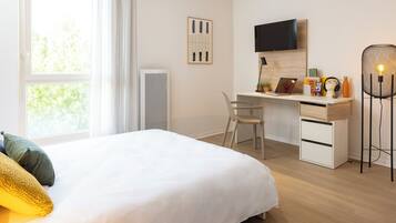 Une chambre d’hôtel équipée d’un lit, d’un bureau avec un ordinateur, d’une chaise, d’une télévision et d’une lampe.