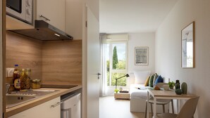 A modern kitchen with a built-in oven, a sink, and a wooden countertop. There is a dining area with a table, chairs, and a window with a view of greenery outside. - Apparteo Montpellier (Montpellier)