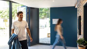 Un hall d’hôtel moderne avec une grande porte vitrée, une plante en pot et une carte accrochée au mur.