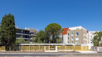 Un moderno edificio residencial de varios pisos, con balcones, una galería techada y un área cercada.