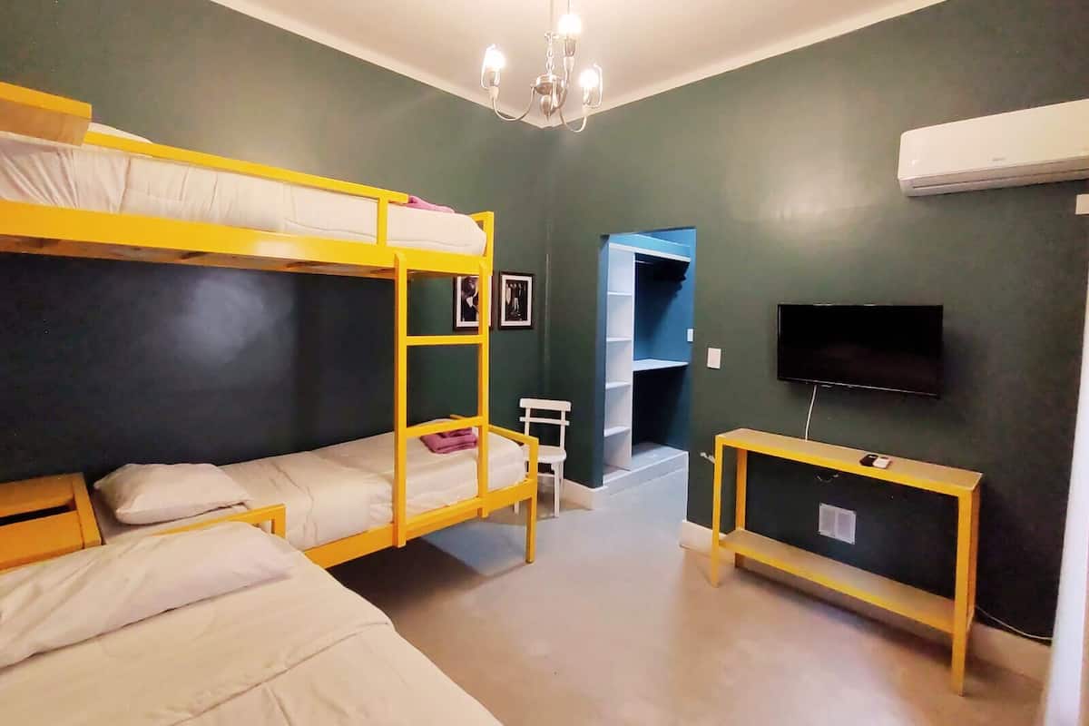 A dorm-style room with bunk beds, a TV, a small table, and a ceiling light.