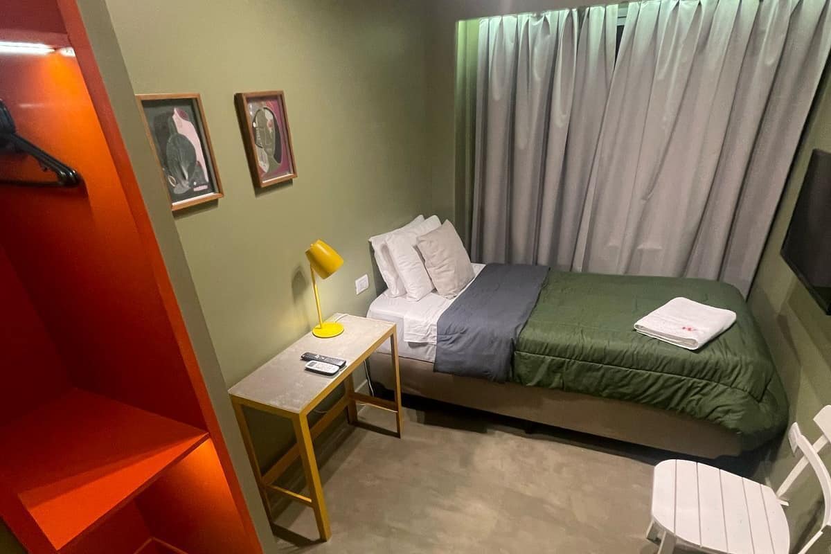 A small, compact bedroom with a bed, a desk, a chair, and a wardrobe.
