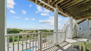 Une terrasse en bois avec une piscine, des rampes blanches et un escalier menant à un espace abrité.