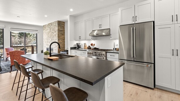 A modern kitchen with white cabinets, a stainless steel refrigerator, a central island with bar stools, and a stone accent wall. - Charming 3BR Mountain Retreat in Silverthorne, CO (Silverthorne)