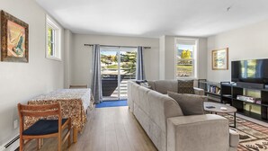 Moderni olohuone, jossa on sohva, ruokapöytä tuoleineen, televisio ja kirjahylly.