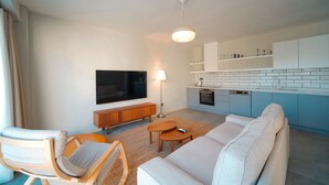 A modern living room with a sofa, armchair, and TV. A kitchen with blue cabinets and a dishwasher is visible. - Bono Premium Collection (Marmaris)