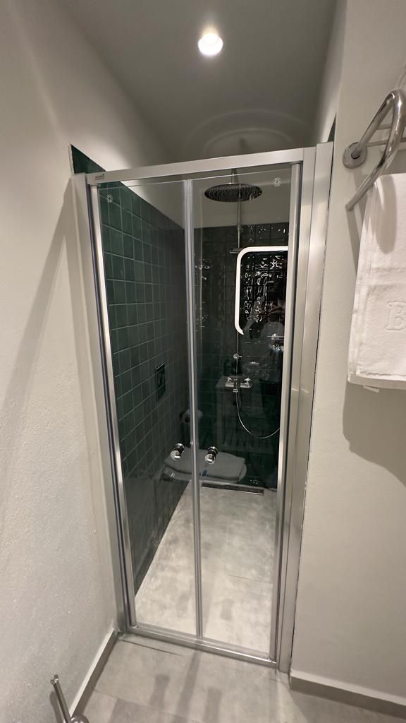 A glass-enclosed shower stall with a tiled wall, a towel rack, and a visible showerhead.
