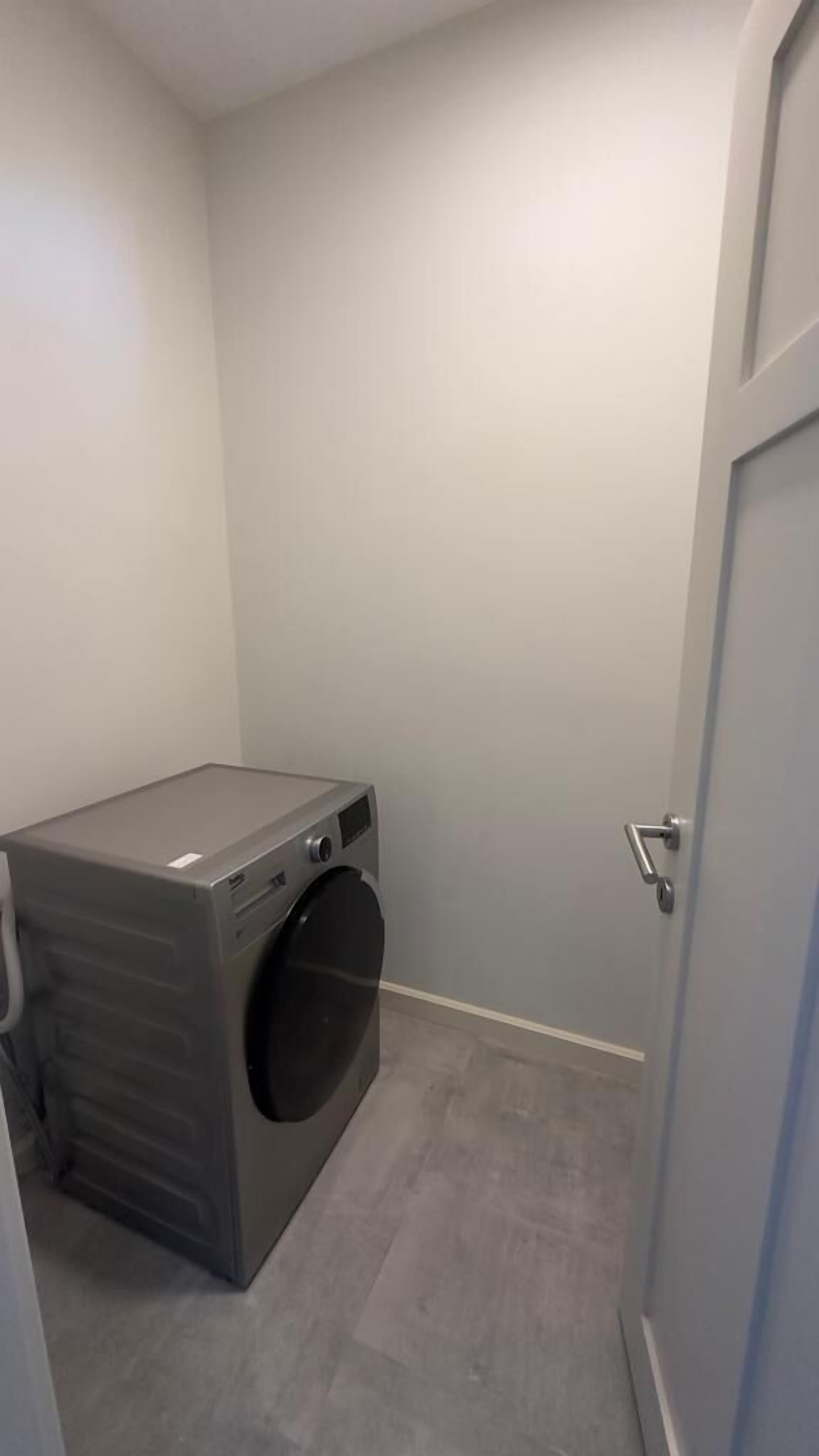 A laundry room with a washing machine, a door, and a light grey wall.
