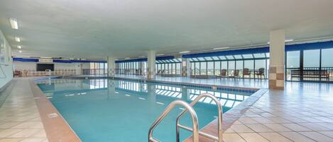 An indoor swimming pool with clear blue water, tiled floor, and a metal pool ladder.