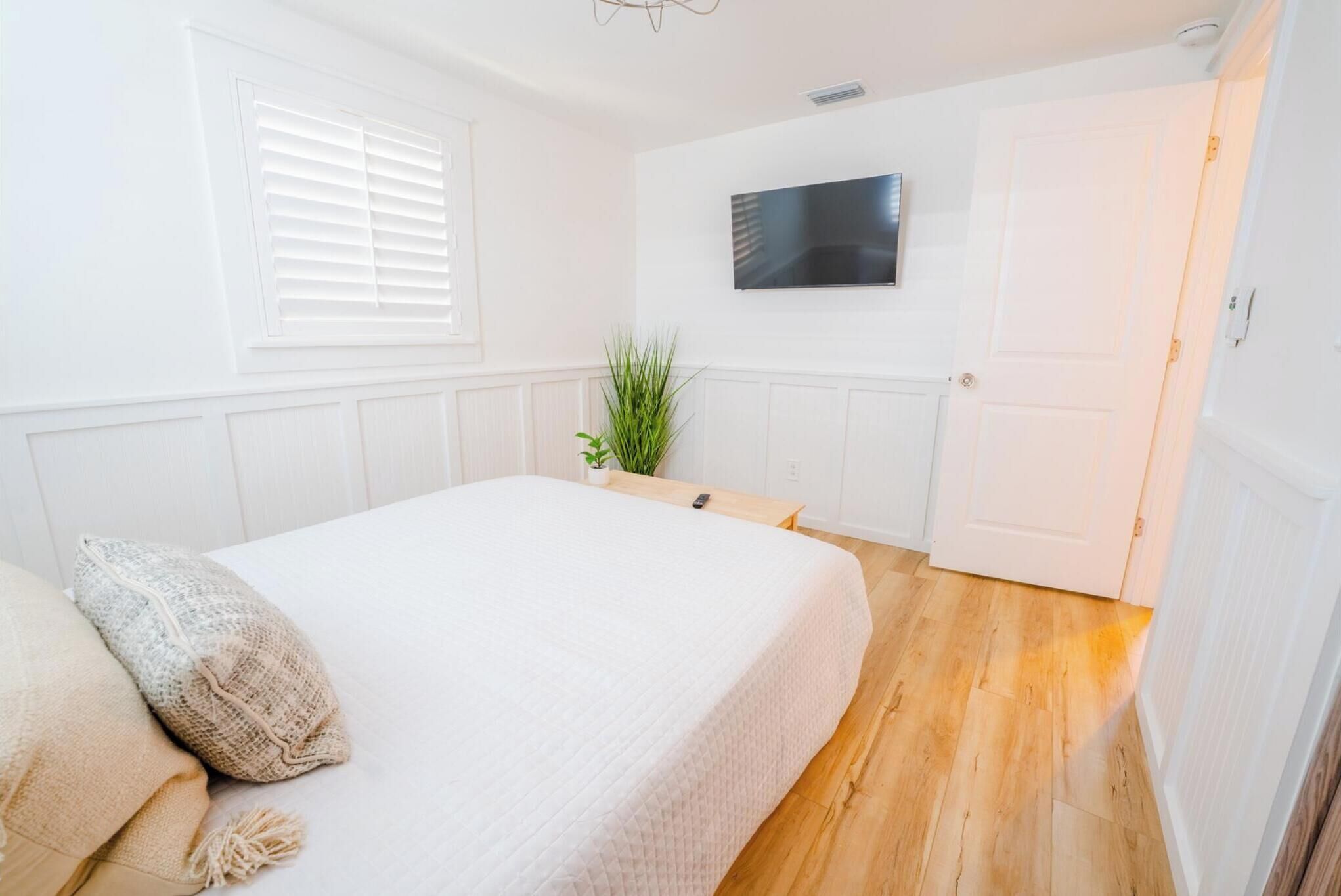 Un dormitorio con cama, televisor en la pared, puerta y ventana con persianas.