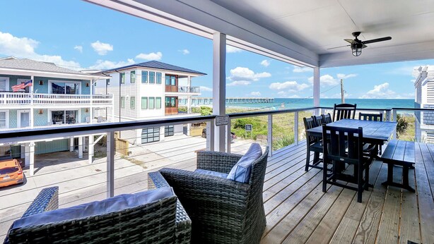 Een overdekt terras buiten met rieten meubels en een tafel, met uitzicht op een strand en zee.