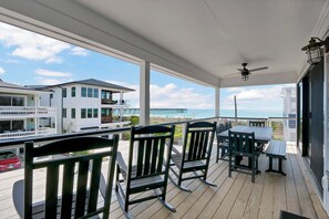A covered outdoor area with a table and chairs, overlooking a beach and a pier.