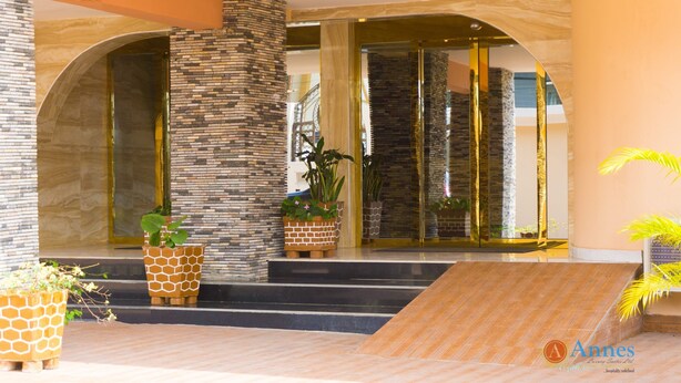 A hotel entrance with a modern design, featuring a stone pillar, glass doors, and potted plants. - Annes luxury suites  (Lagos)