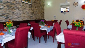 A restaurant with red upholstered chairs, tables with floral tablecloths, and orange flowers in vases. - Annes luxury suites  (Lagos)