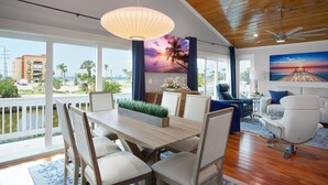 A spacious living area with a wooden ceiling, a dining table with chairs, a sofa, and a TV displaying a sunset scene. - Canal Front- Easy Walk to Beach- 2BR Flip Flops Forever (Fort Myers Beach)