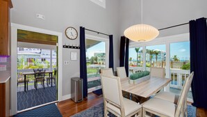 A dining area with a wooden table and chairs, a clock on the wall, and a view of the outside. - Canal Front- Easy Walk to Beach- 2BR Flip Flops Forever (Fort Myers Beach)