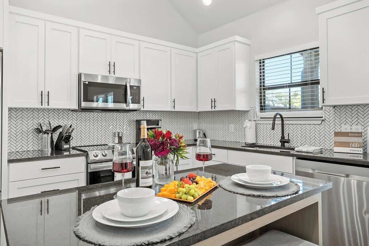 A modern kitchen with white cabinets, stainless steel appliances, and a herringbone tile backsplash.