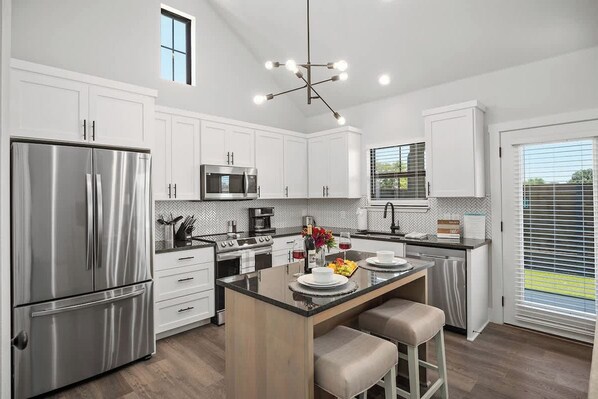 Una cocina moderna con armarios blancos, electrodomésticos de acero inoxidable y una isla central con asientos.
