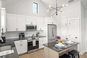 A modern kitchen with white cabinets, stainless steel appliances, a central island, and a pendant light.