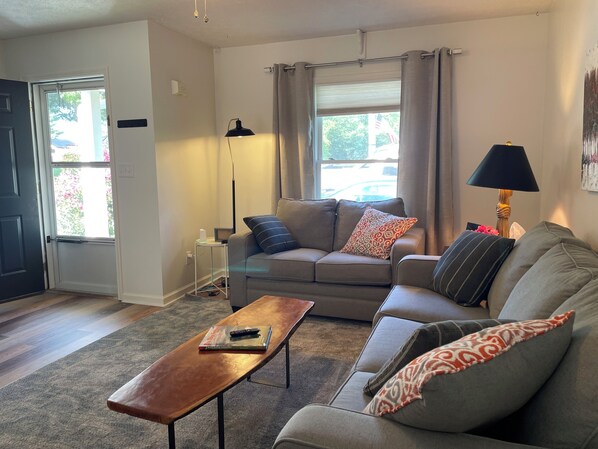 A living room with a sofa, a coffee table, a lamp, and a window with curtains. - Quiet mountain retreat convenient to hiking and Asheville (Weaverville)