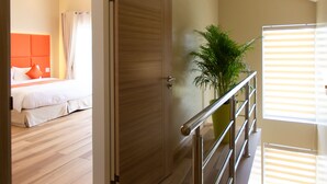 Quarto de hotel moderno com soalho de madeira, cama com roupa de cama branca e uma planta verde.