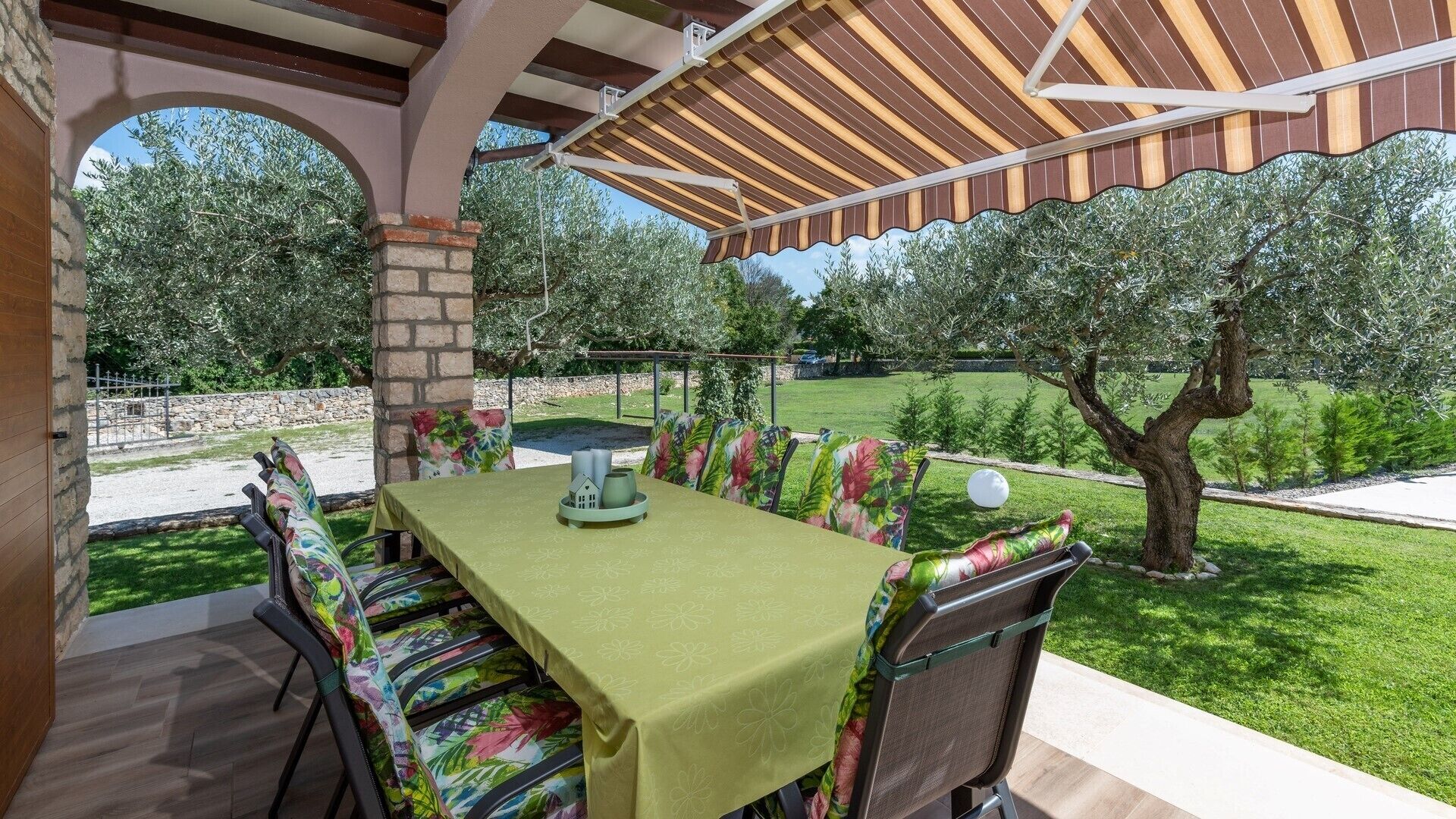 An outdoor patio with a table set for four, surrounded by chairs with floral upholstery, under a wooden pergola.