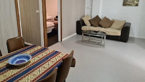A room with a dining table, chairs, a sofa, and a glass coffee table. - Orchard Apartment Devonport (Don)