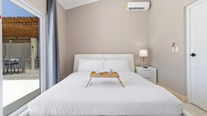 Ein Hotelzimmer mit einem Bett, einem Nachttisch mit Lampe, einem Fenster mit Blick auf einen Außenbereich und einer Klimaanlage an der Wand.
