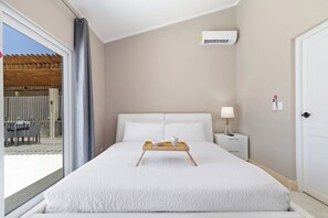 Een hotelkamer met een bed, een nachtkastje met een lamp, een raam met uitzicht op een buitengebied en een airconditioner aan de muur.