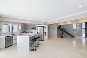 Une cuisine moderne dotée d’un îlot central, de tabourets de bar, d’appareils électroménagers en acier inoxydable et d’un escalier menant à un niveau supérieur.