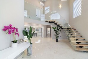 Un intérieur moderne avec un escalier en verre, un comptoir d’accueil blanc et des plantes en pot.