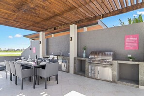 Eine Terrasse im Freien mit einem Esstisch für vier Personen, einem Grill und einem kleinen Spülbecken.