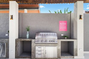 A barbecue grill with a stainless steel finish, a small potted plant, and a sign with safety rules.