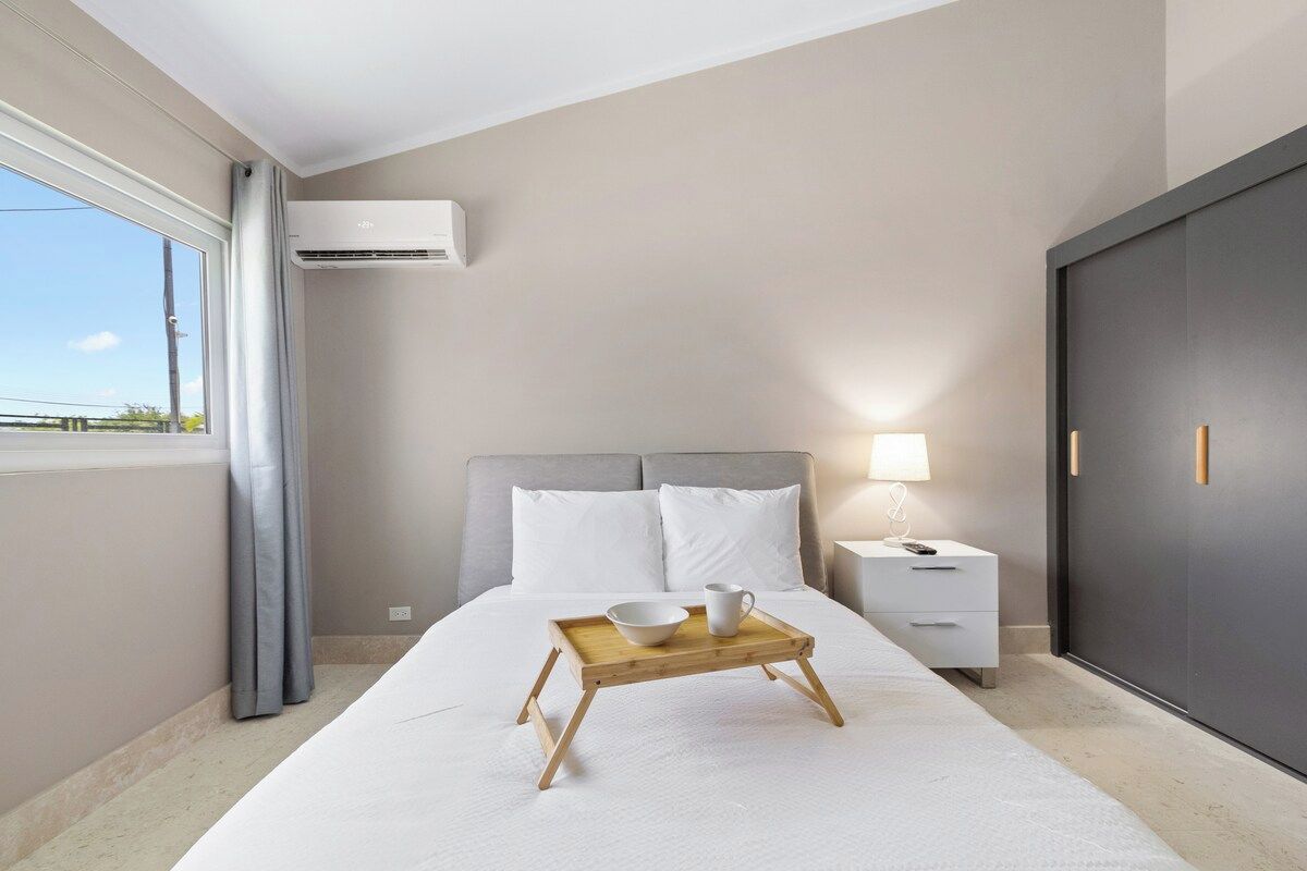 Un dormitorio con cama, mesita de noche, lámpara y ventana con cortinas.