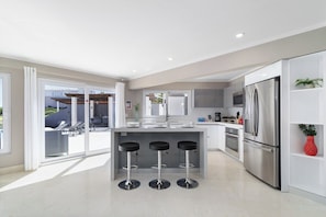 Een moderne keuken met een centraal eiland, barkrukken, roestvrijstalen apparatuur en een schuifdeur naar een buitenruimte.