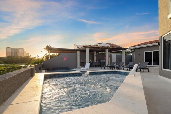 A swimming pool with a sunken area, lounge chairs, and a covered seating area.