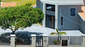 Un bâtiment moderne à deux étages, doté d’un balcon, d’un arbre devant et d’une entrée fermée par un portail.