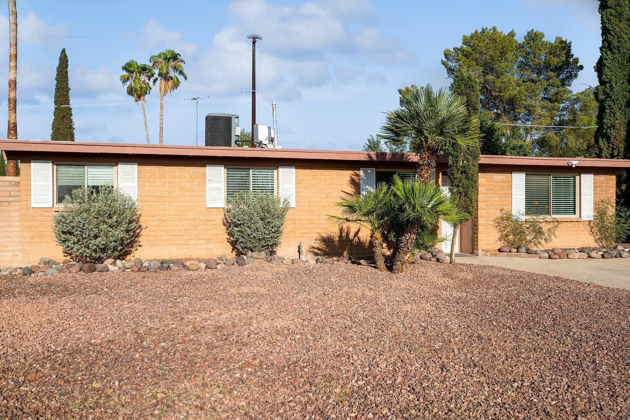 A two-story building with a brick facade, white shutters, and a gravel driveway.