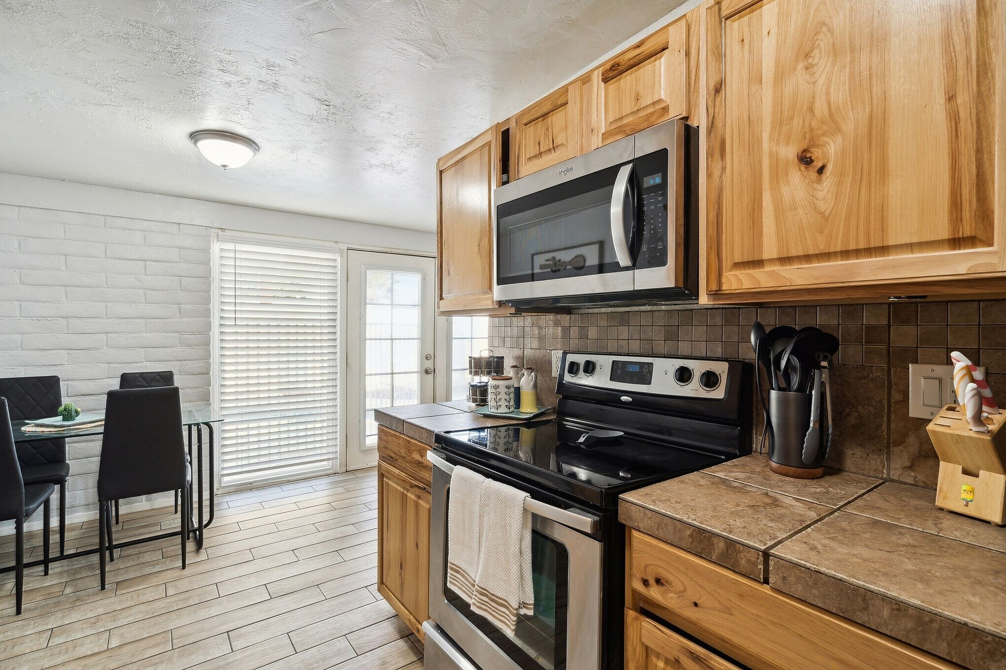 A kitchen with wooden cabinets, a microwave, a stove, and a dining area with a table and chairs.