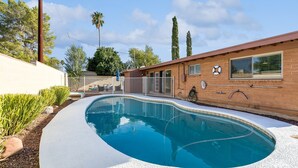 Une piscine avec un bâtiment en briques en arrière-plan, entourée d’une clôture et agrémentée d’un aménagement paysager.