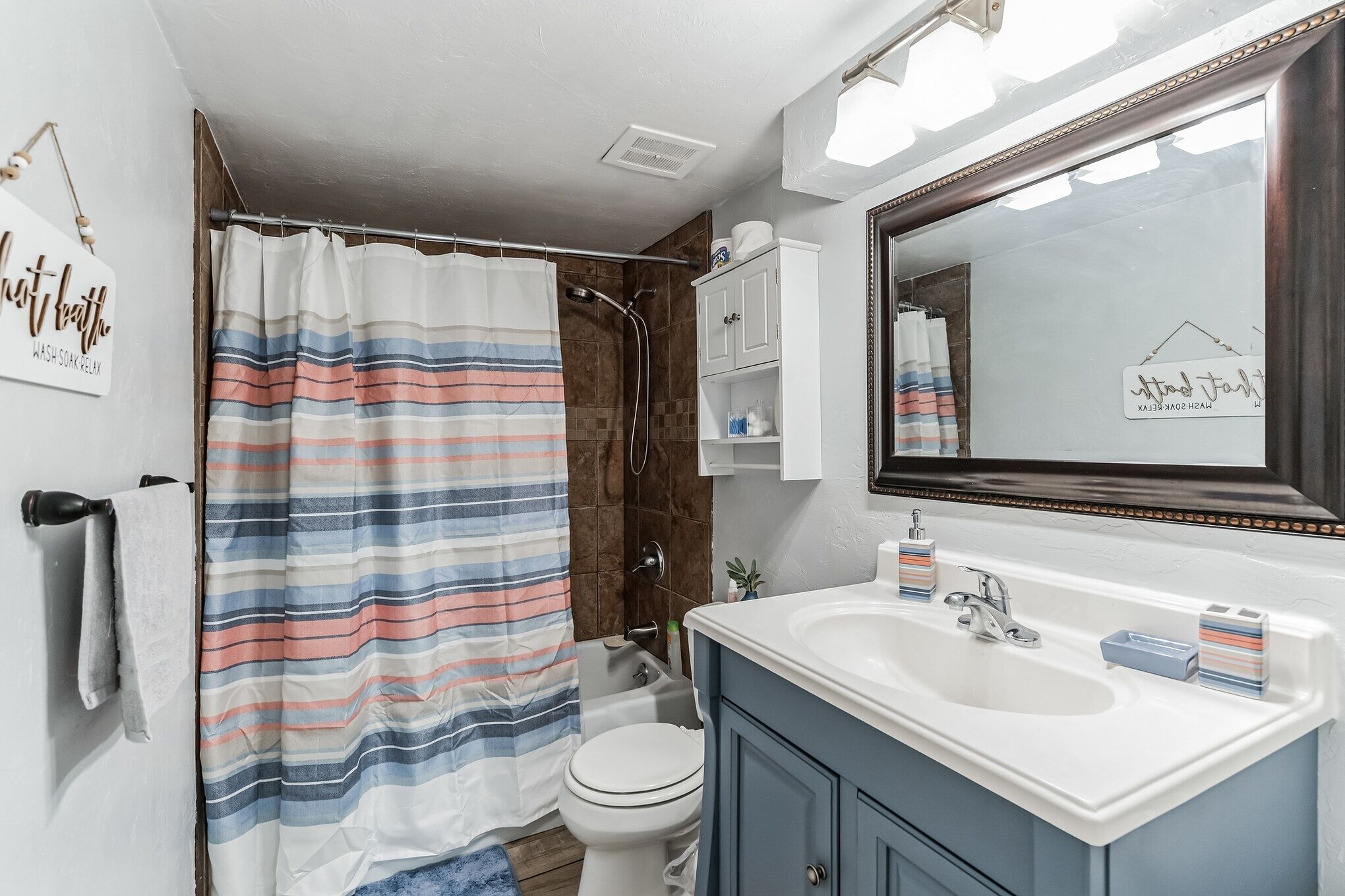 Une salle de bain avec un rideau de douche à rayures, des toilettes blanches, un lavabo avec un miroir au-dessus et un meuble contenant des articles de toilette.